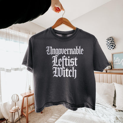 Dark grey t-shirt with white text &amp;quot;Ungovernable Leftist Witch&amp;quot; on a hanger.