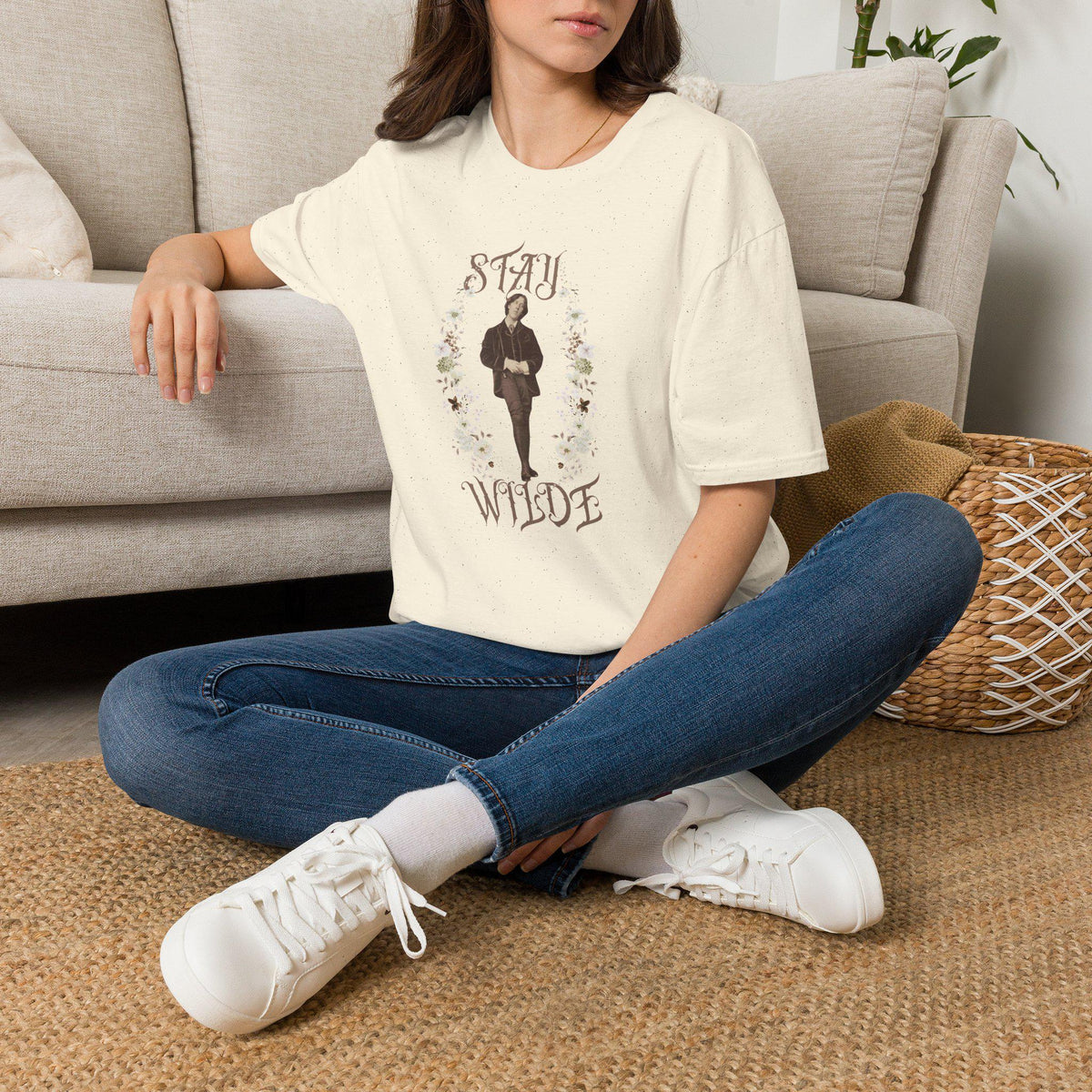 May include: A cream-colored short-sleeve t-shirt featuring a central graphic of a person in a suit surrounded by a floral wreath. The text &amp;quot;STAY&amp;quot; appears above the figure and &amp;quot;WILDE&amp;quot; below, both in a decorative serif font on the fabric.