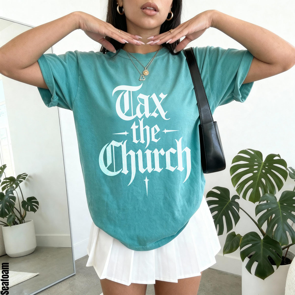 Teal t-shirt with white &amp;quot;Tax the Church&amp;quot; gothic text, worn by a person with a black purse.