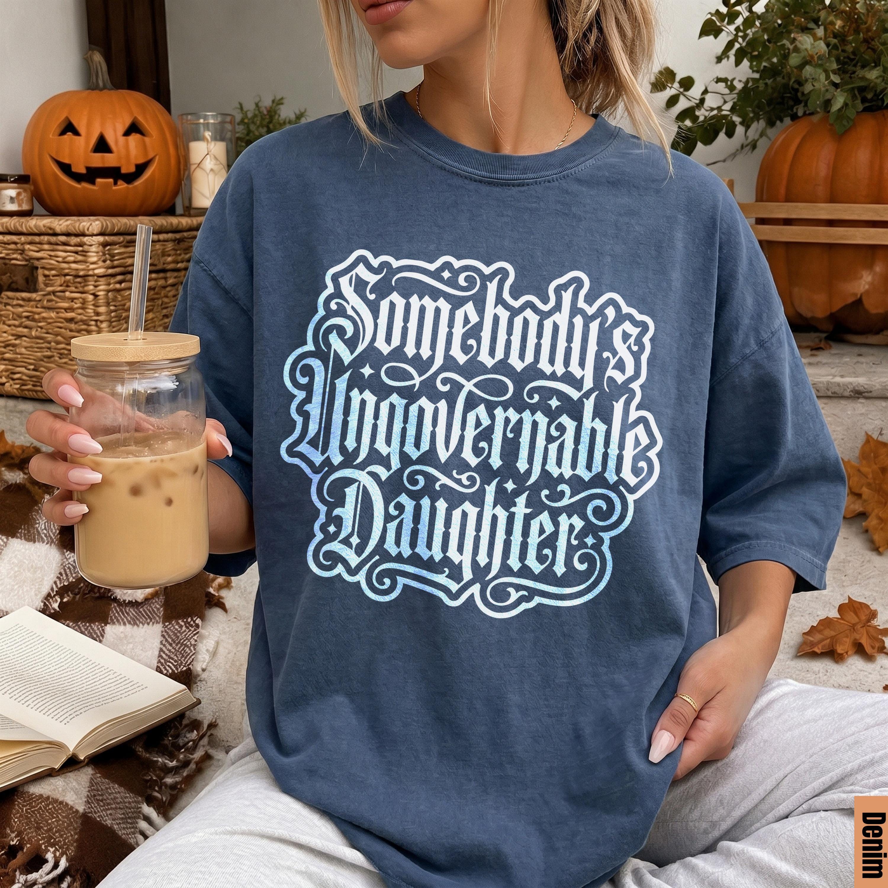 Blue t-shirt with white text &amp;quot;Somebody Ungovernable Daughter&amp;quot; and Halloween decor.