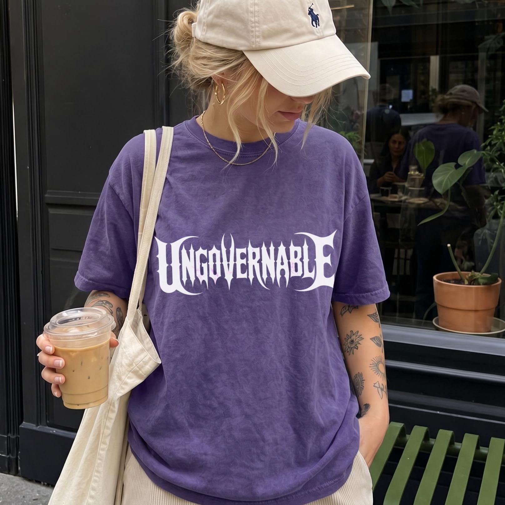 Woman in purple t-shirt with &amp;quot;UNGOVERNABLE&amp;quot; text, holding coffee.