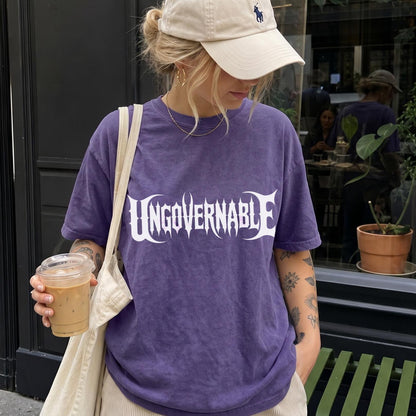 Woman in purple t-shirt with &amp;quot;UNGOVERNABLE&amp;quot; text, holding coffee.