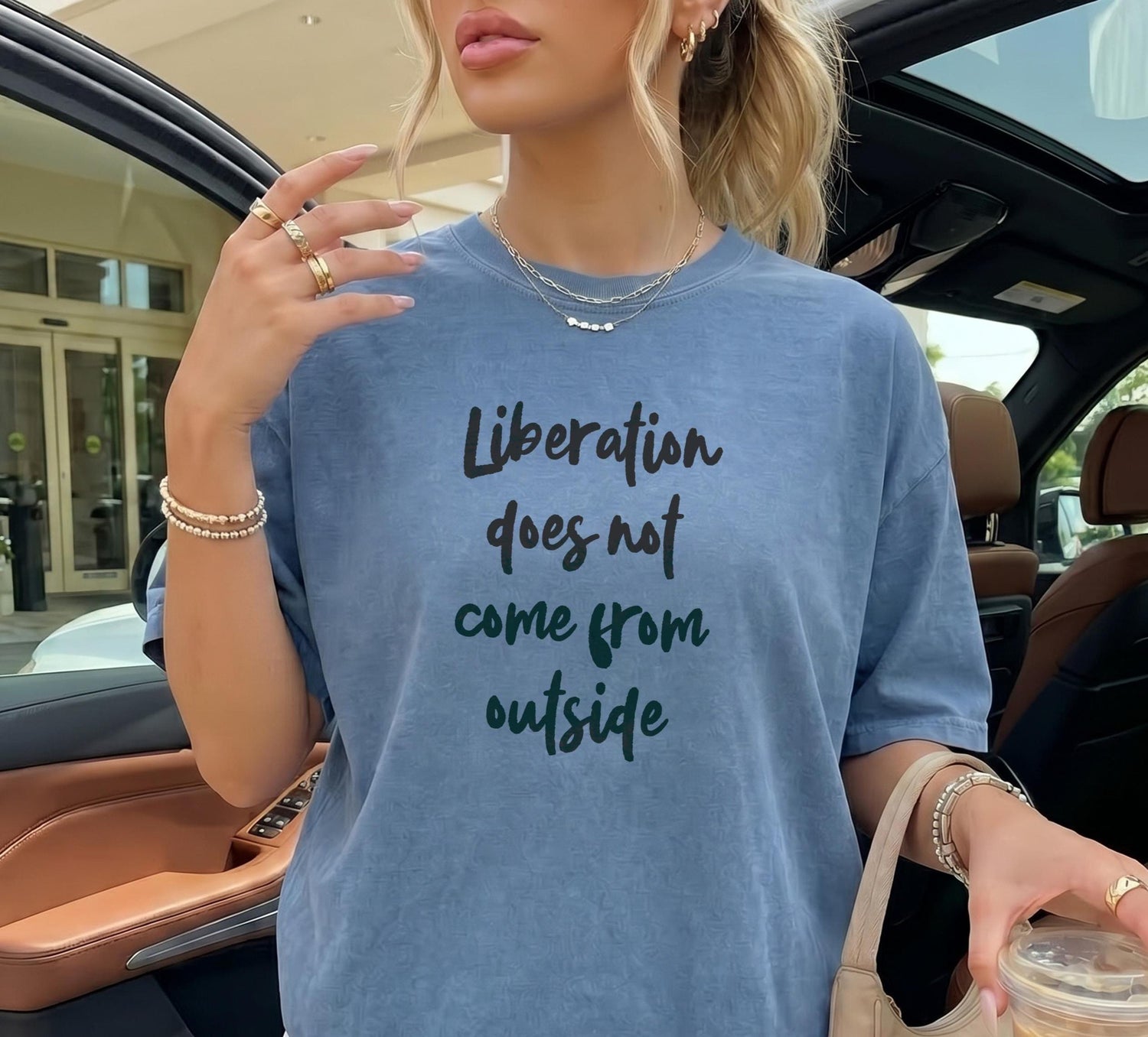 Blue t-shirt with &amp;quot;Liberation does not come from outside&amp;quot; text, held by a person in a car.