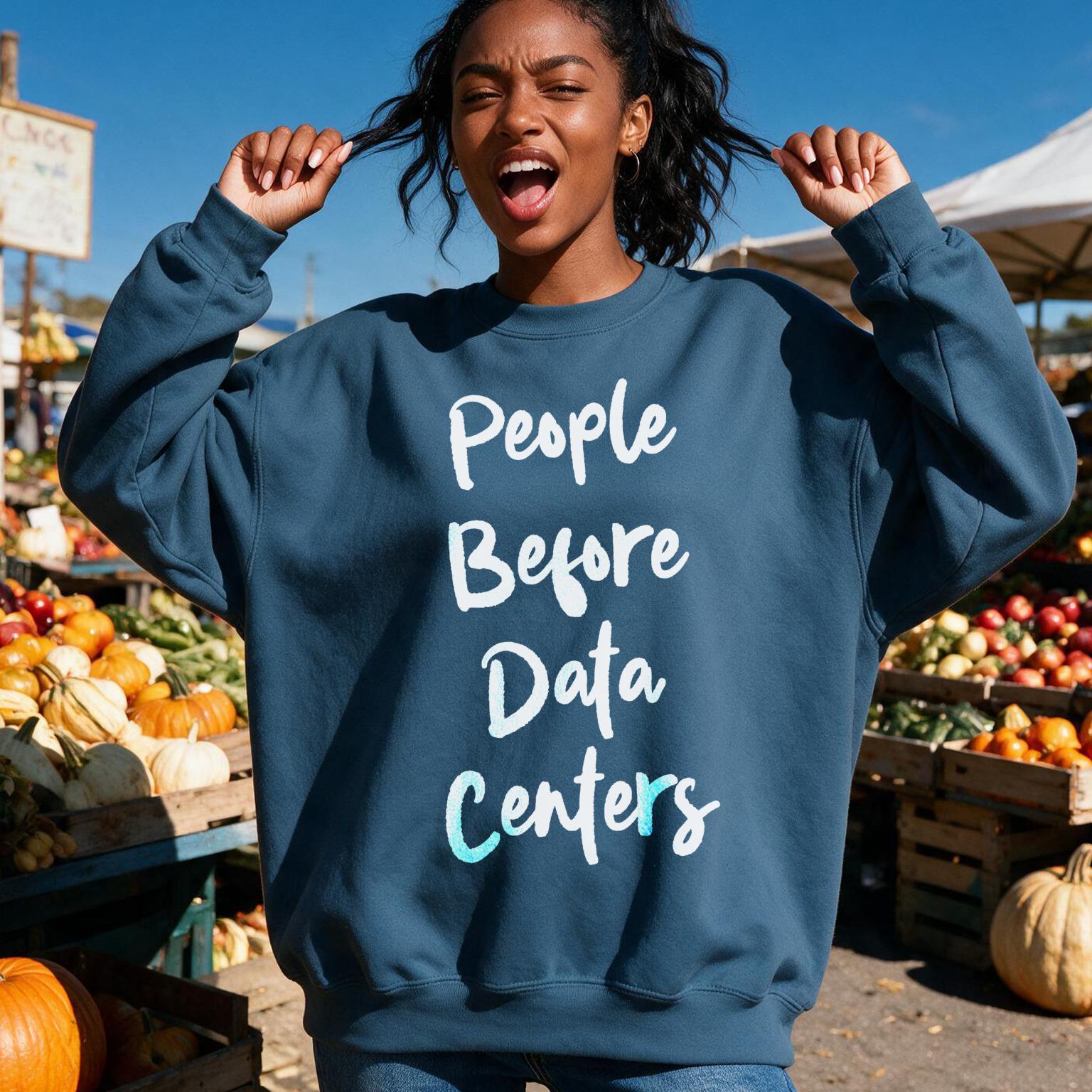 Woman in navy sweatshirt with &amp;quot;People Before Data Centers&amp;quot; text, outdoor market background.