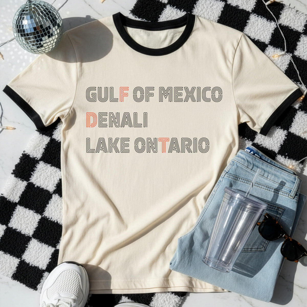 Cream ringer t-shirt with &amp;quot;Gulf of Mexico,&amp;quot; &amp;quot;Denali,&amp;quot; and &amp;quot;Lake Ontario&amp;quot; text.