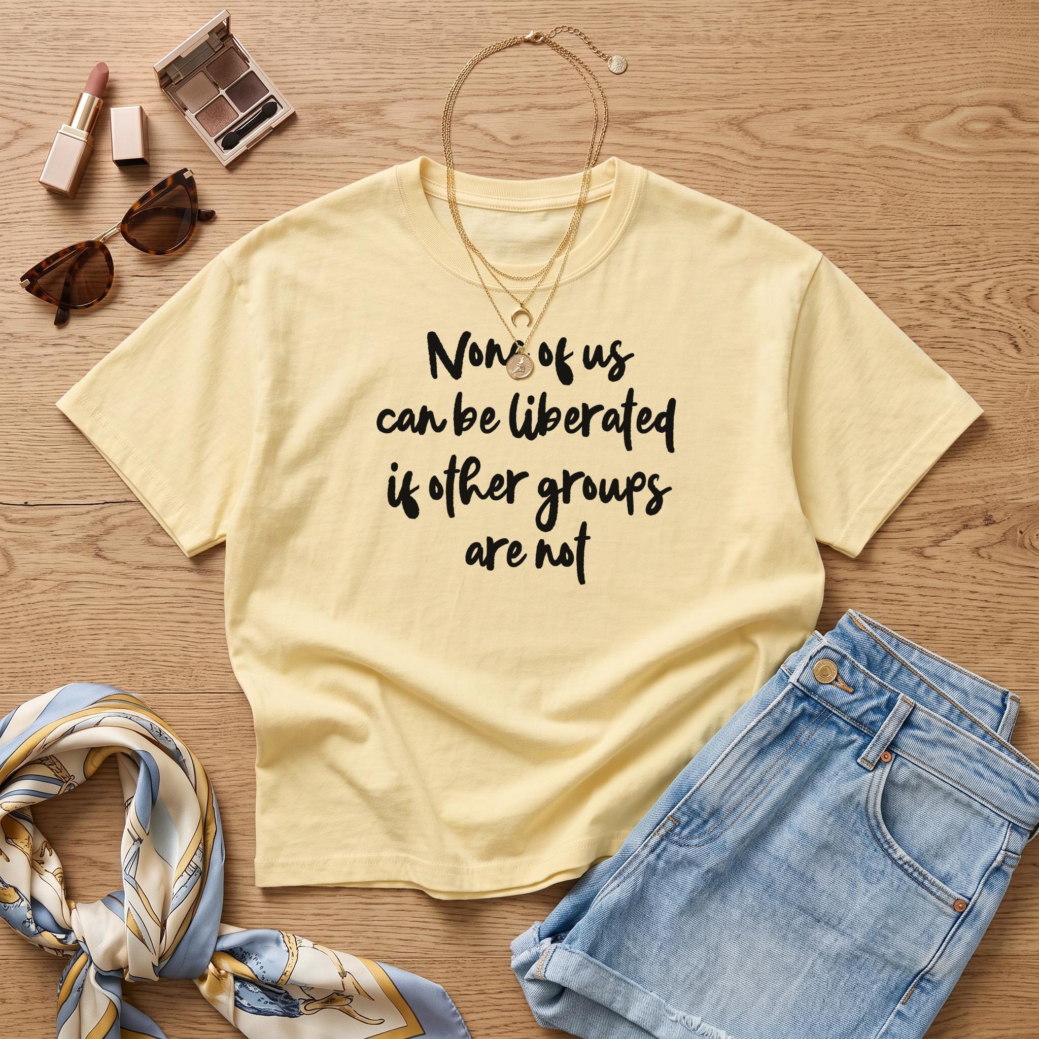 Pale yellow t-shirt with &amp;quot;None of us can be liberated if other groups are not&amp;quot; text.