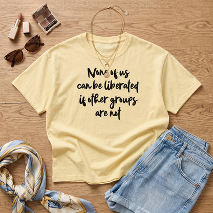 Pale yellow t-shirt with &amp;quot;None of us can be liberated if other groups are not&amp;quot; text.