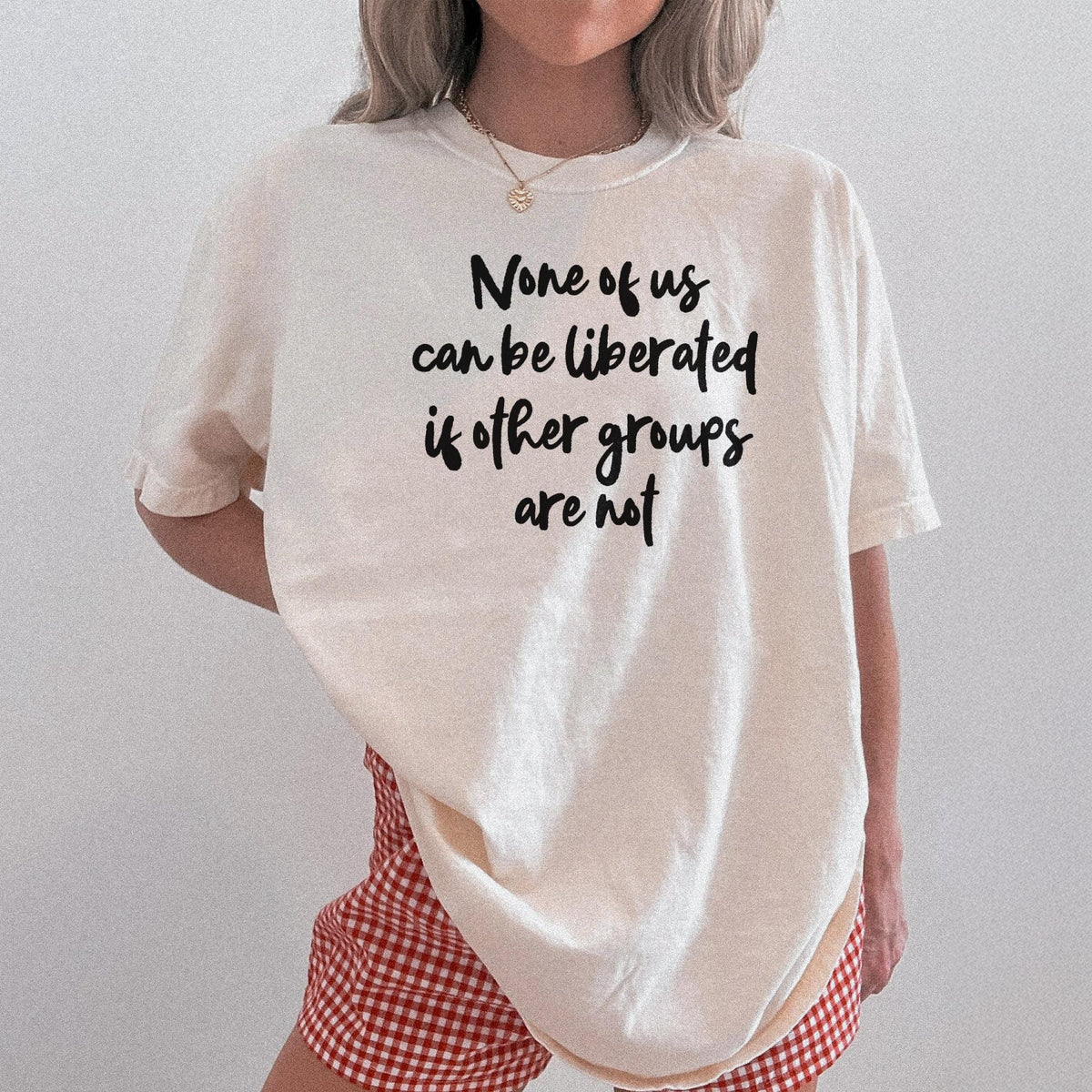 Cream t-shirt with black text &amp;quot;None of us can be liberated if other groups are not.&amp;quot;