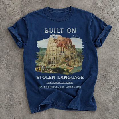 Blue t-shirt with artwork of Tower of Babel and text &amp;quot;BUILT ON STOLEN LANGUAGE&amp;quot;.