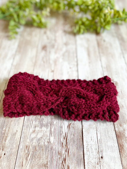 A red, Virginia-raised merino ear warmer rests on a wood plank with greenery in the background
