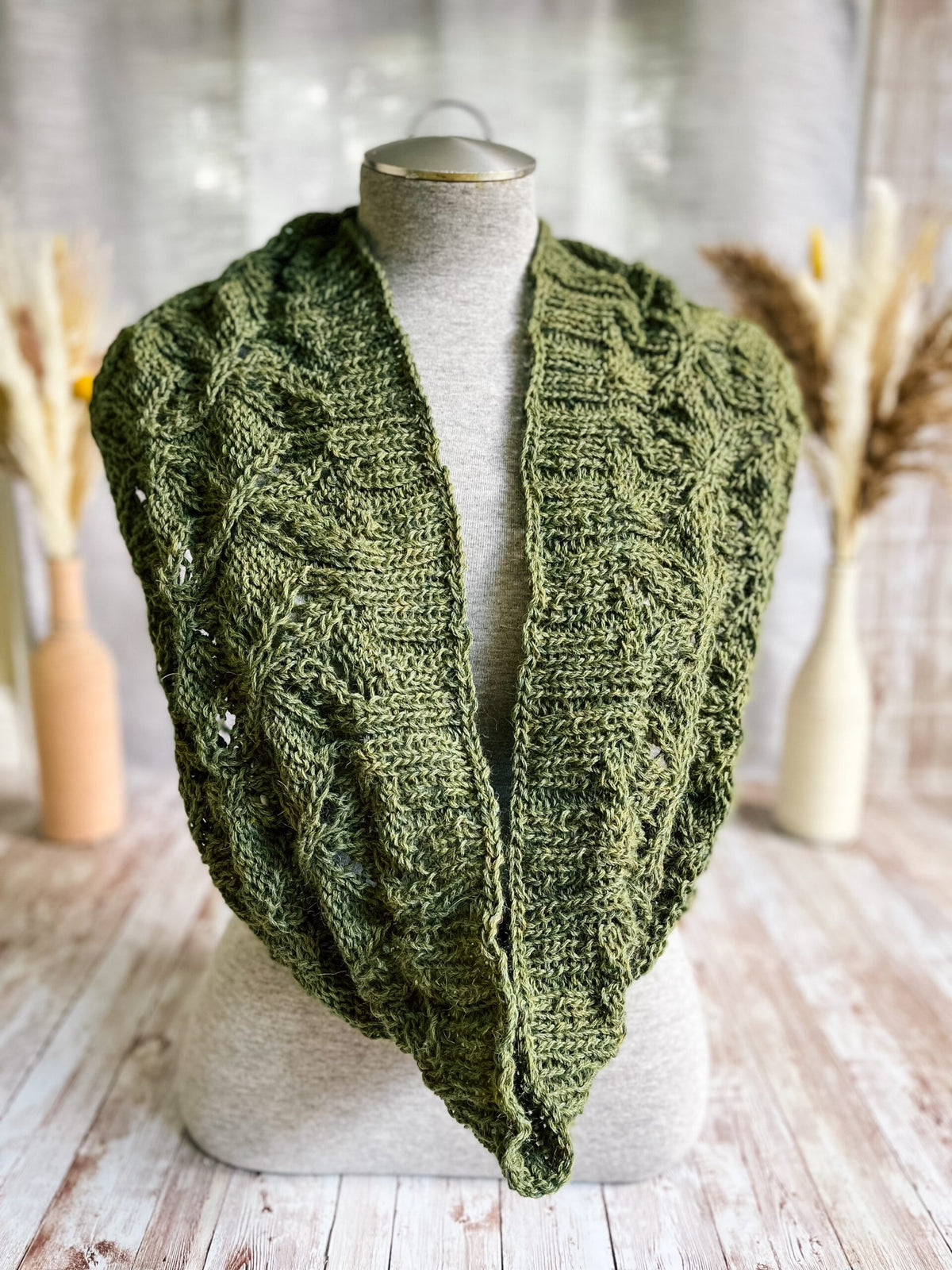 A gray mannequin torso displays a green infinity scarf, hand-knit in a cables and lace pattern