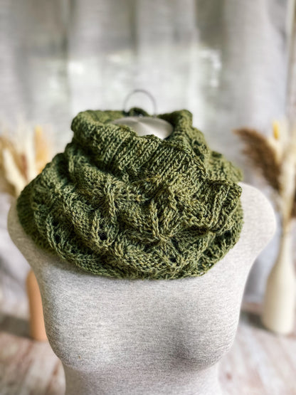 A gray mannequin torso displays a green cowl, hand-knit in a cables and lace pattern