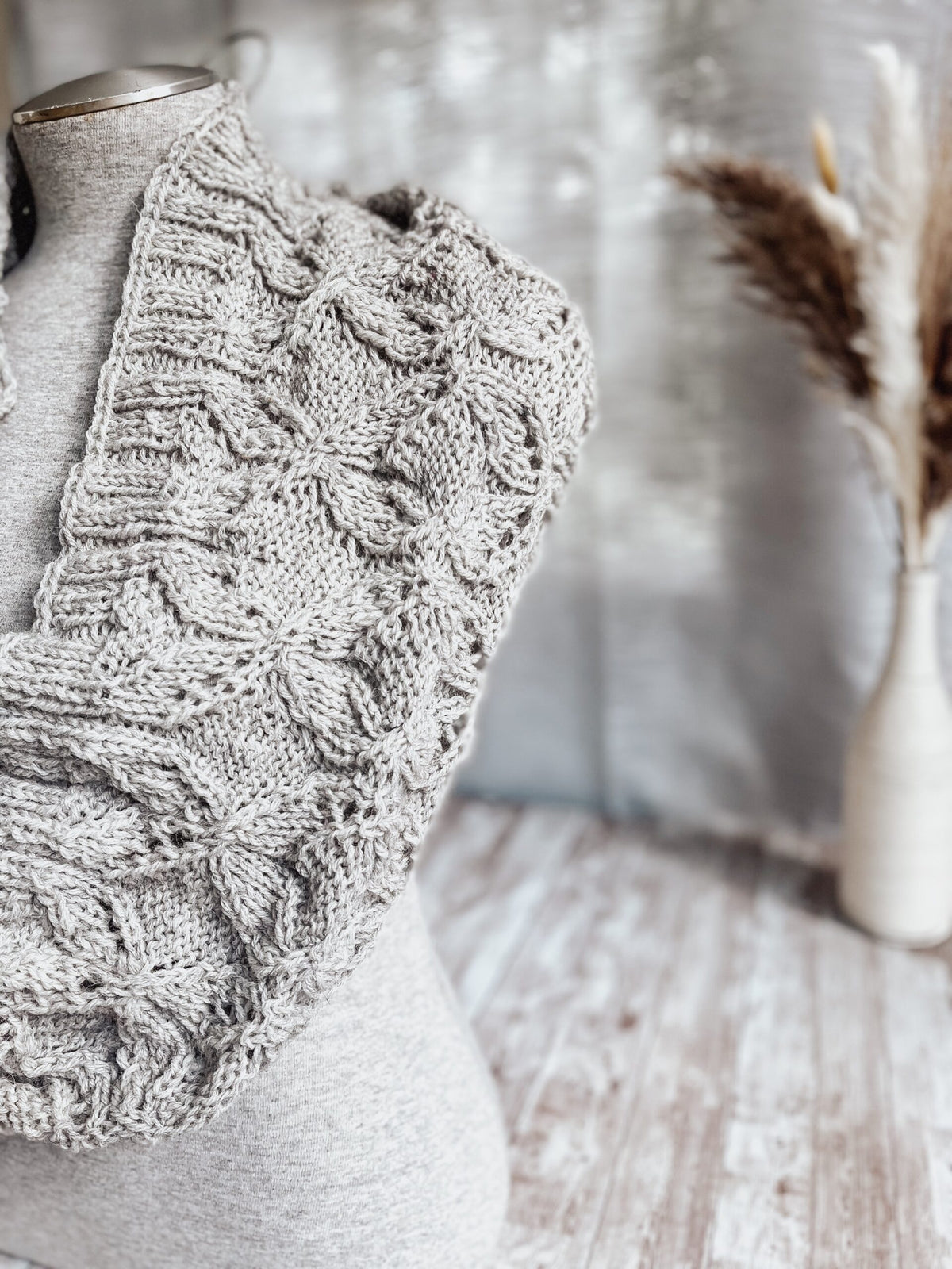 A gray mannequin torso displays a gray infinity scarf, hand-knit in a cables and lace pattern