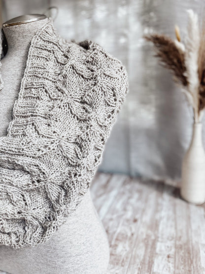 A gray mannequin torso displays a gray infinity scarf, hand-knit in a cables and lace pattern