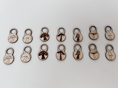 A total of 14 wood stitch markers with a variety of hand-drawn mushroom designs are displayed on a white background.