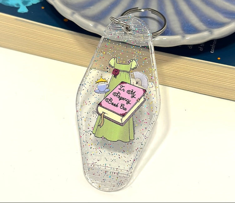 Inspired by the romance of the Regency Era, this whimsical hand drawn empire dress is paired with trinkets of the time including a cute teacup, tiara and fan! 📖 ☕ ✨👑 Perfect motel keychain for any bookish babe. Pair it with the matching sticker!