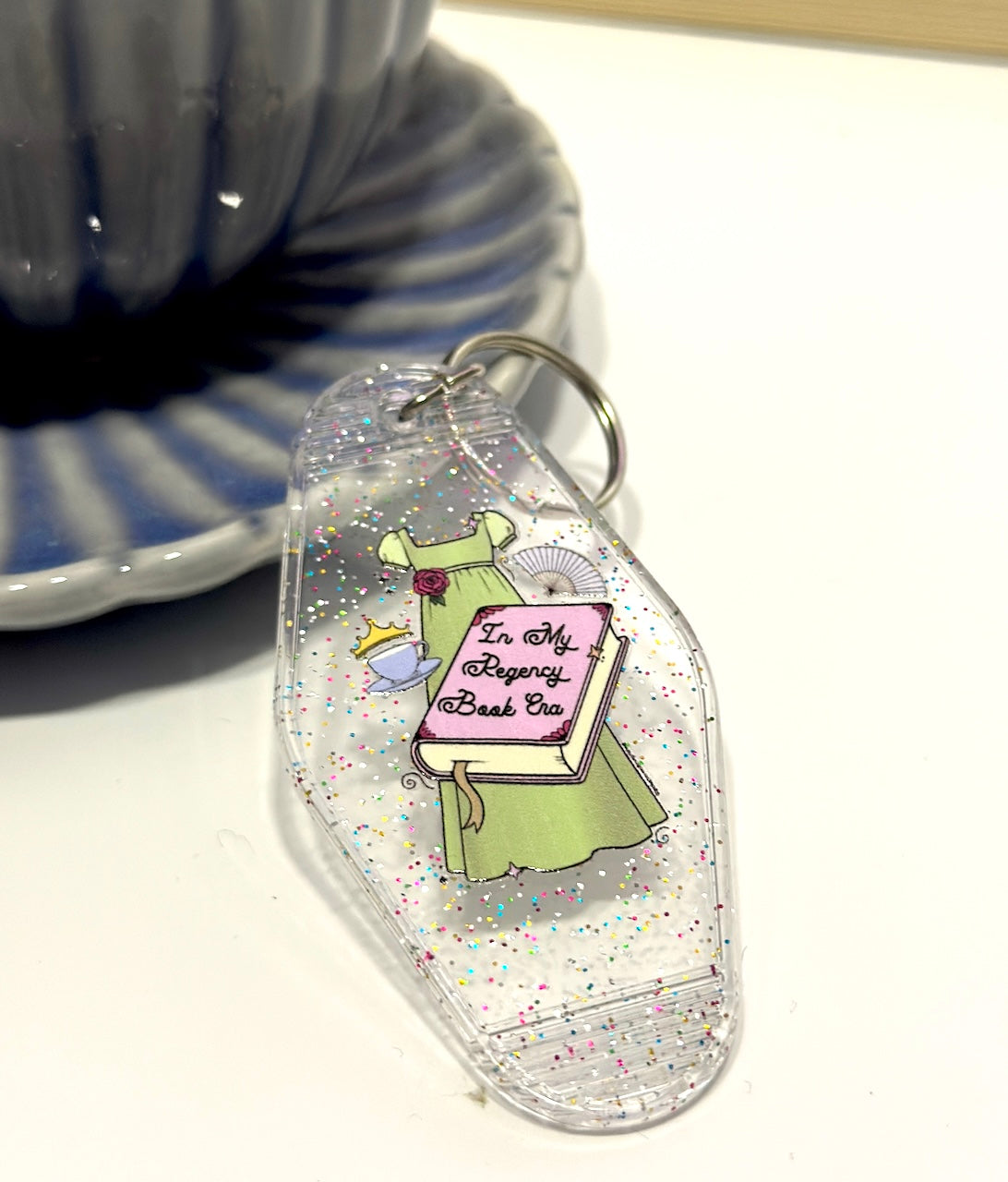 Inspired by the romance of the Regency Era, this whimsical hand drawn empire dress is paired with trinkets of the time including a cute teacup, tiara and fan! 📖 ☕ ✨👑 Perfect motel keychain for any bookish babe. Pair it with the matching sticker!