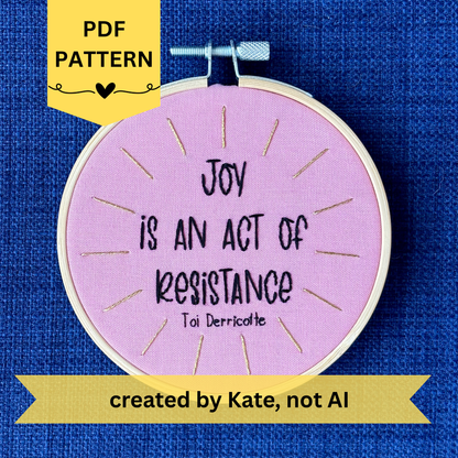 PDF pattern created by Kate, not AI. "Joy is an act of resistance" - Toi Derricotte. Text is a handwriting font and hand embroidered in black embroidery thread. Words are centered in a burst of golden, metallic rays. Fabric is light pink cotton. Framed as wall art or christmas ornament in light wood embroidery hoop.