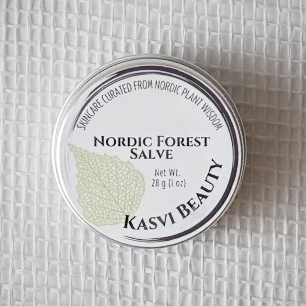 A round silver tin of Kasvi Beauty Nordic Forest Salve on a textured white woven background. The lid is white with black text and a light green birch leaf illustration.