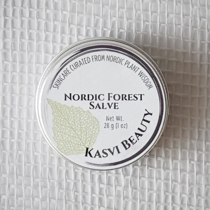 A round silver tin of Kasvi Beauty Nordic Forest Salve on a textured white woven background. The lid is white with black text and a light green birch leaf illustration.