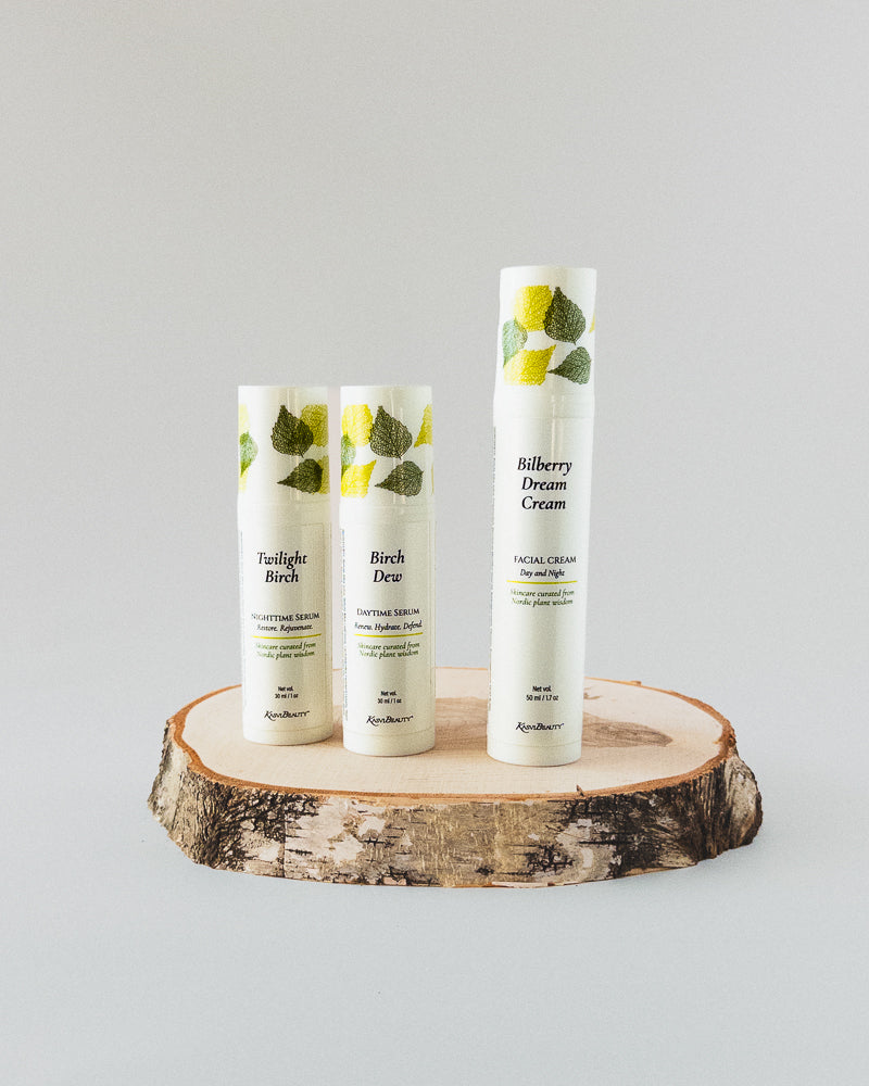 Three white skincare bottles from Kasvi Beauty displayed on a rustic wood slice against a light gray background. The bottles feature green leaf illustrations and labels for &