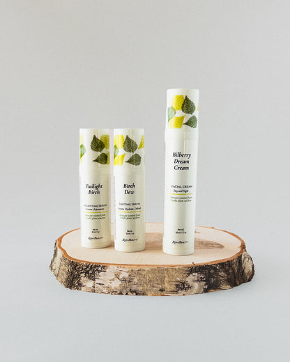 Three white skincare bottles from Kasvi Beauty displayed on a rustic wood slice against a light gray background. The bottles feature green leaf illustrations and labels for &