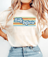 A woman wearing a cream-colored t-shirt with a retro-style graphic that reads &