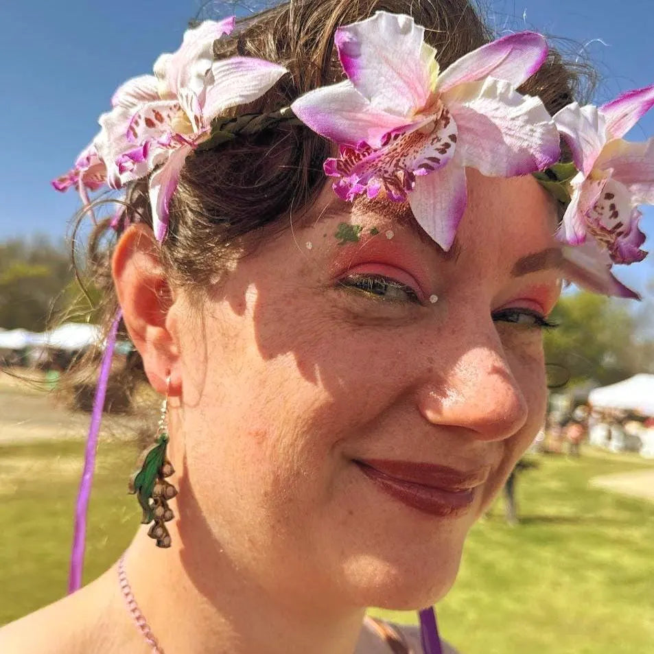 Lifestyle photo of woman wearing hand-painted wooden lily of the valley dangle earrings with green leaves and white bell flowers and hypoallergenic sterling silver hooks, delicate floral statement jewelry at outdoor festival