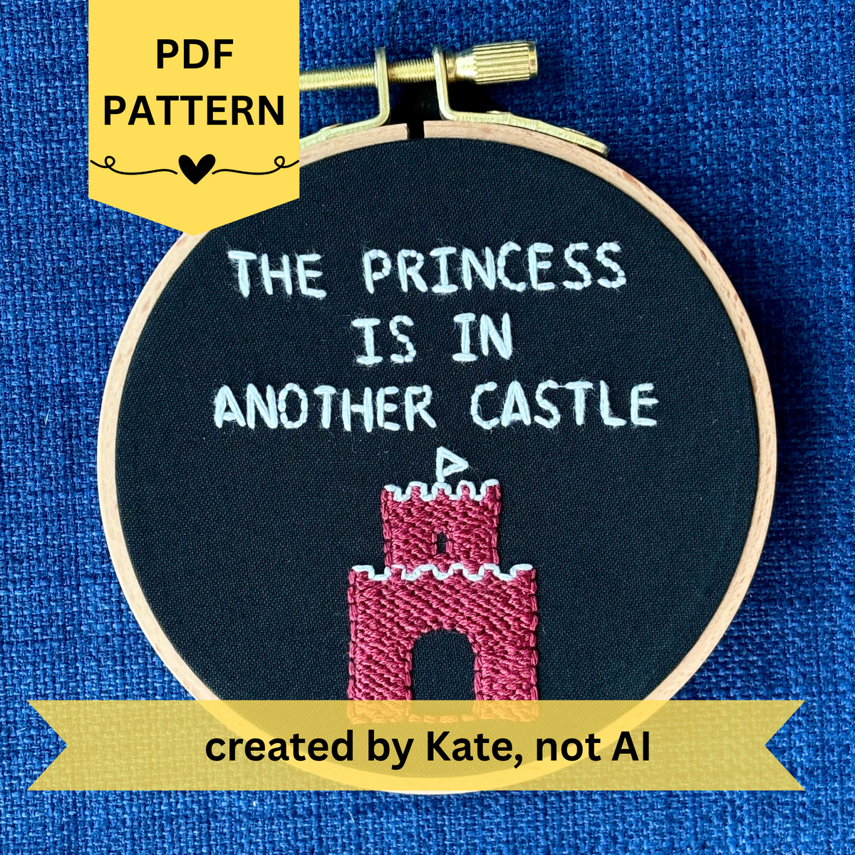 PDF pattern created by Kate, not AI. Embroidery hoop reads, "The princess is in another castle. Text is all capital letters in sans serif font and hand embroidered in white. Below the words is a brick castle with a triangular white flag on the top. Hand stitched on black cotton. Framed in light wood embroidery hoop and displayed as wall art or DIY handmade Christmas ornament.