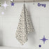 Warm gray atomic starburst mid century modern tea towel hanging from a chrome hook against white subway tile, showing full pattern of charcoal and gray starburst motifs on a natural oatmeal cotton twill background