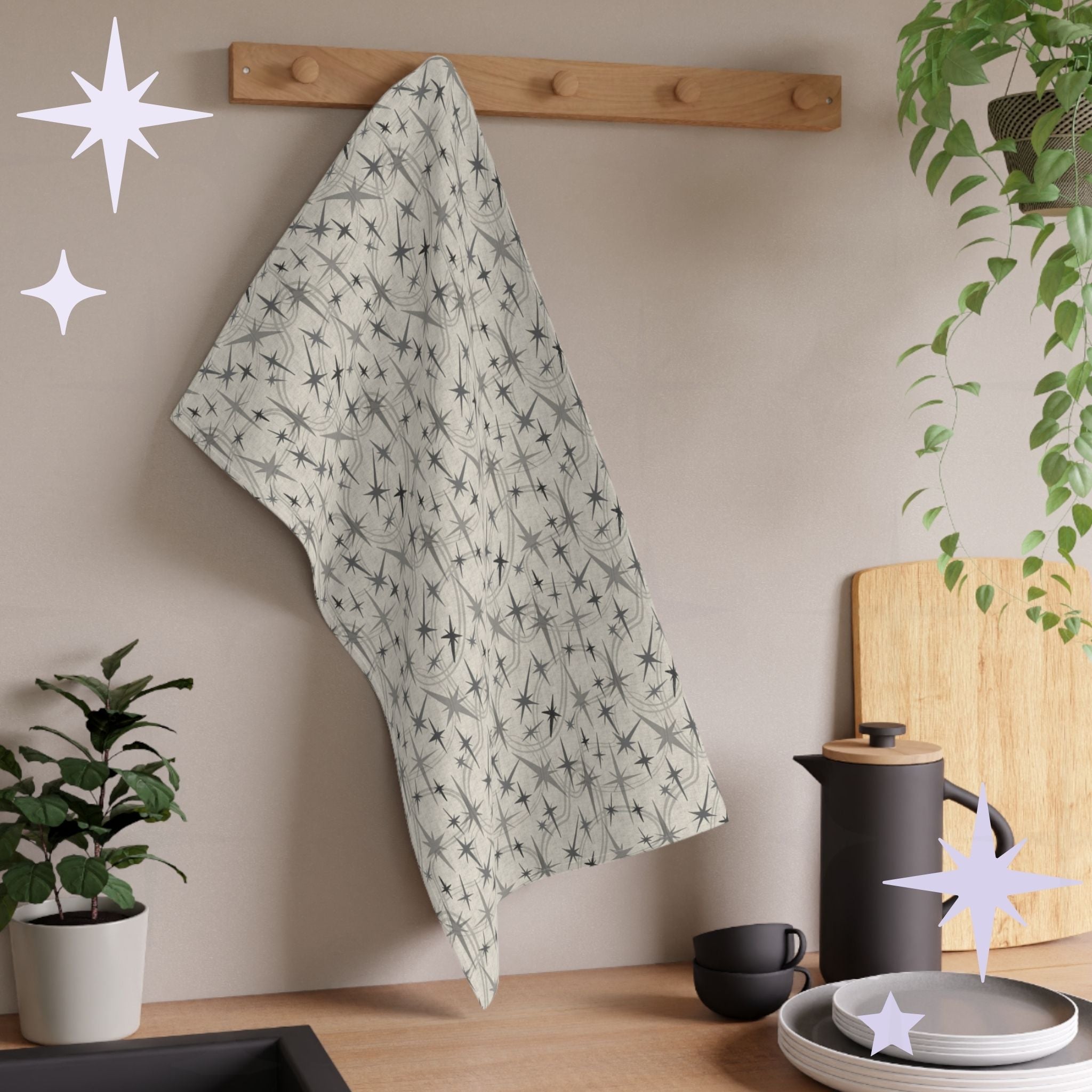 Warm gray mid century modern tea towel draped over a wooden rack against white shiplap wall with decorative star shapes and a pine plant in a black pot