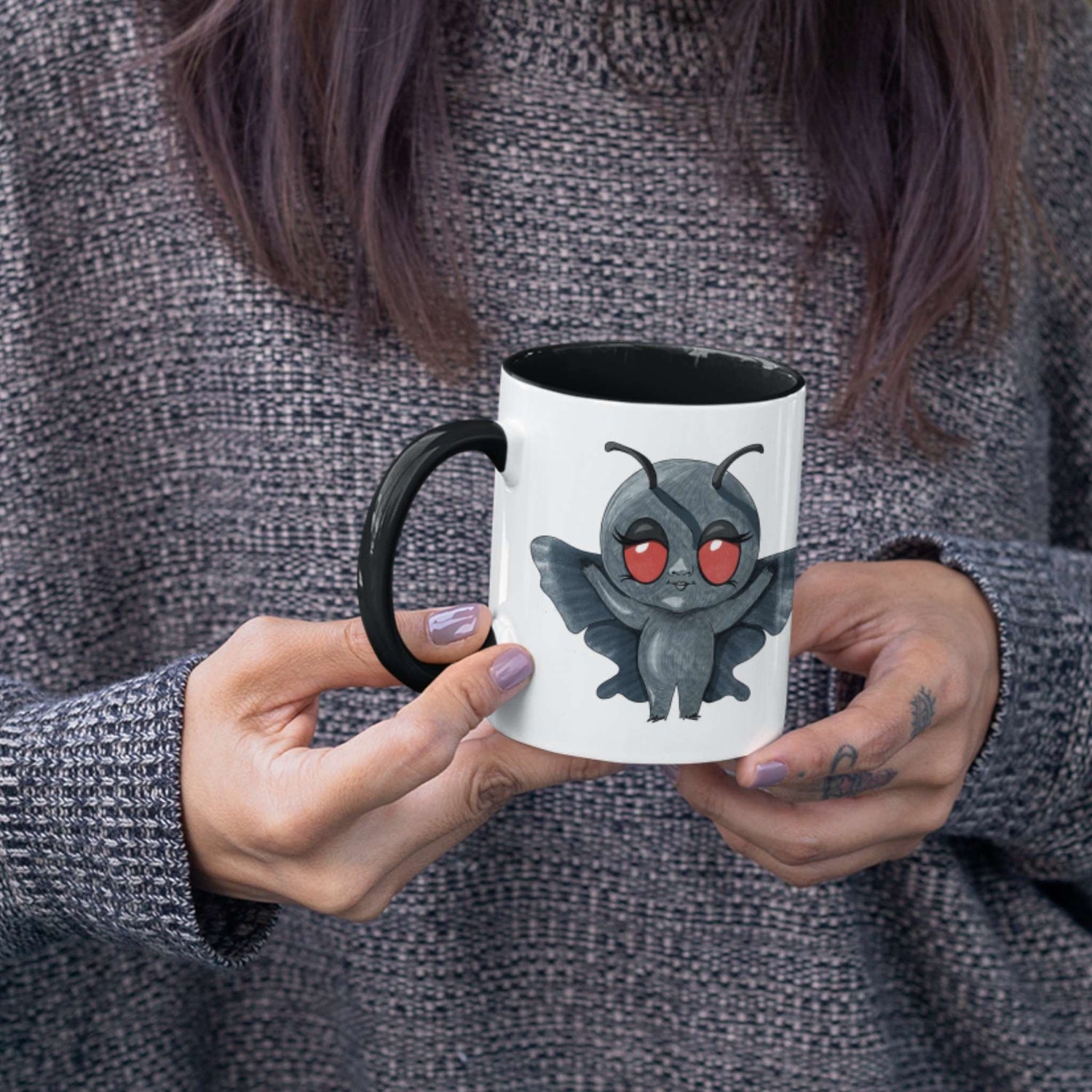 Person in a gray sweater holding the cute Mothman cryptid mug