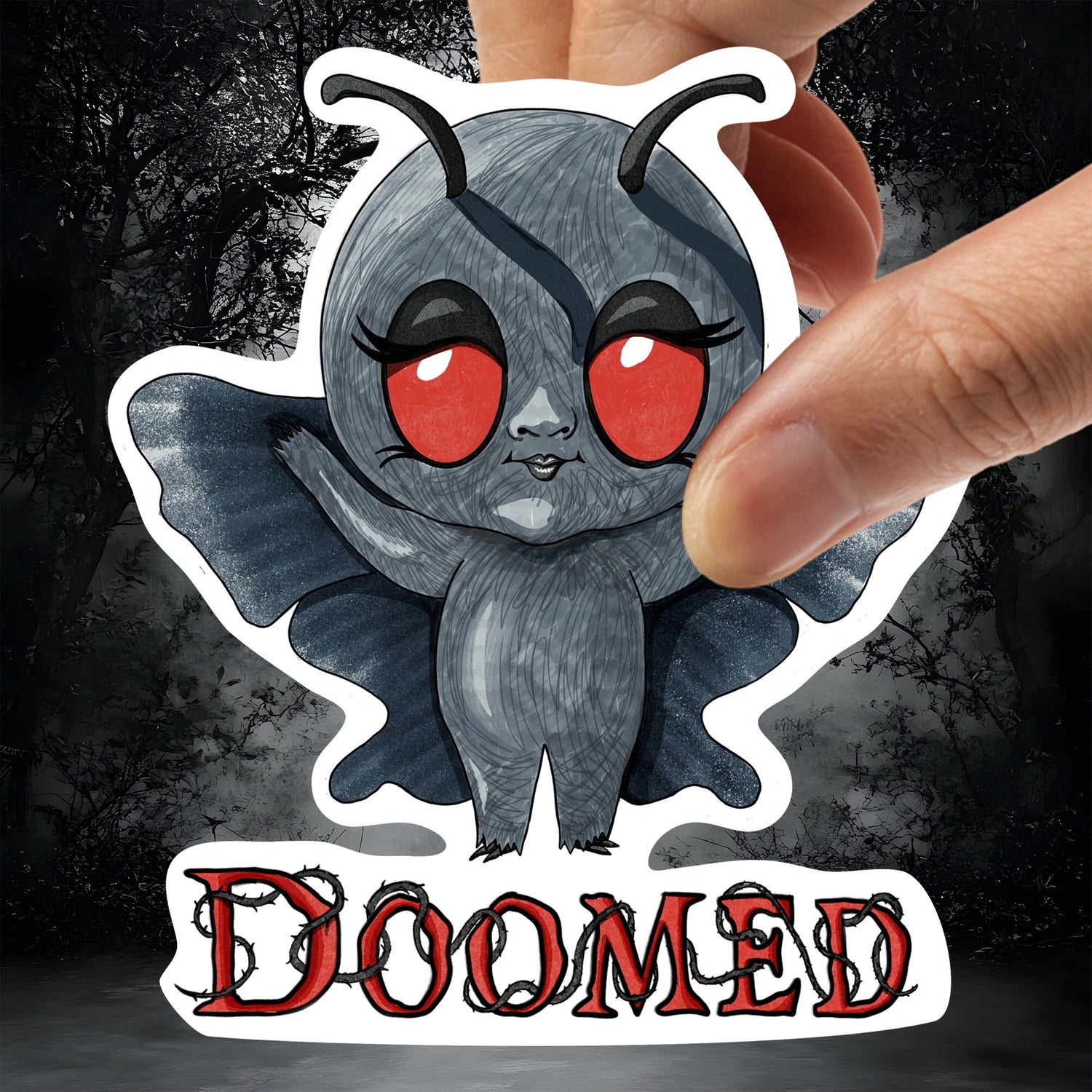 Hand holding the Mothman sticker against a dark misty forest background