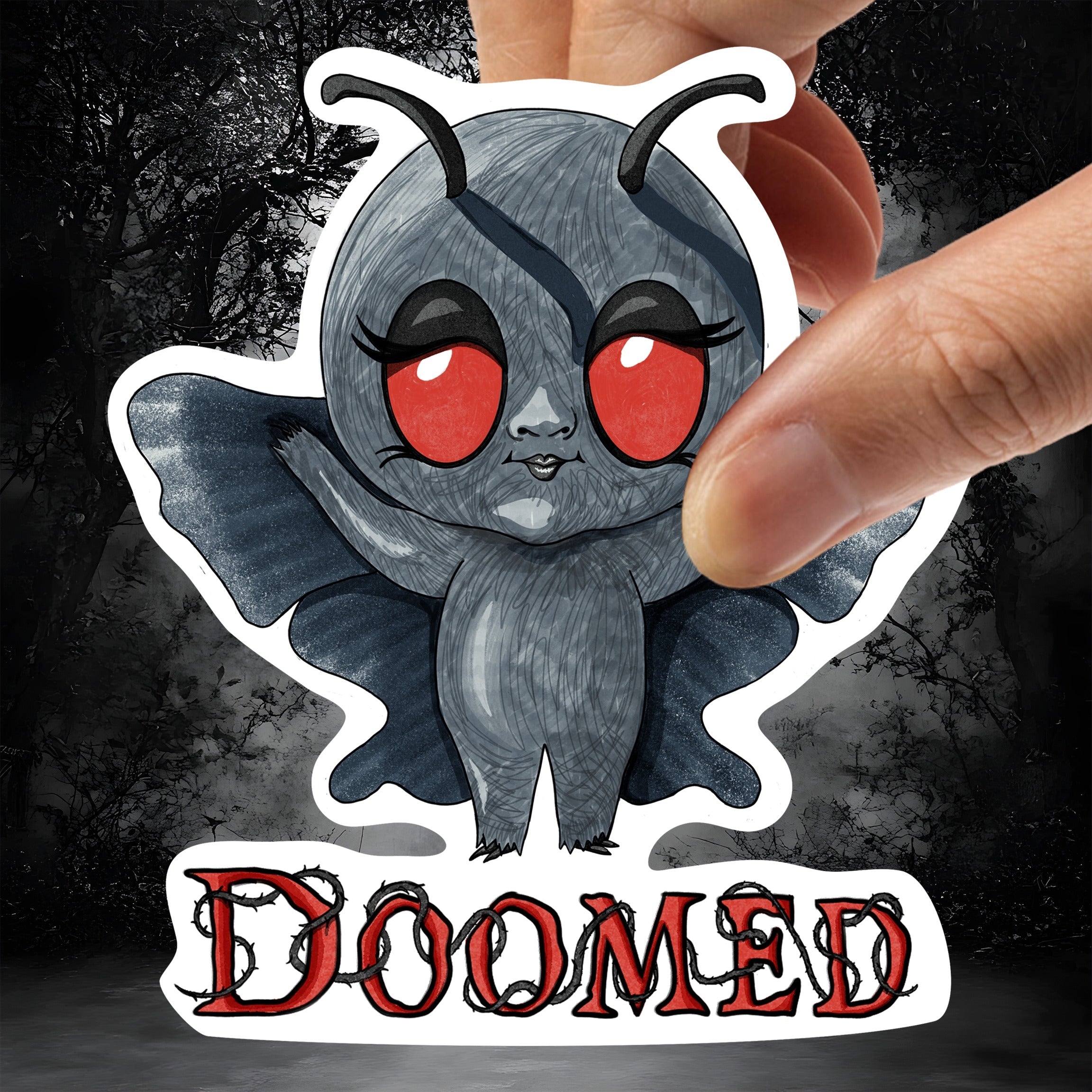 Hand holding the Mothman sticker against a dark misty forest background