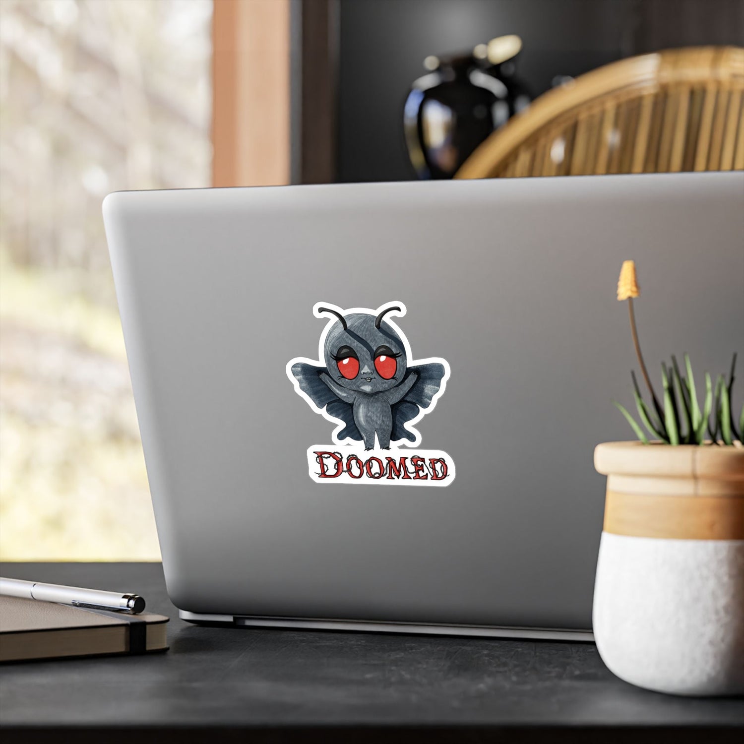 Medium Mothman cryptid sticker on the back of a silver laptop by a window