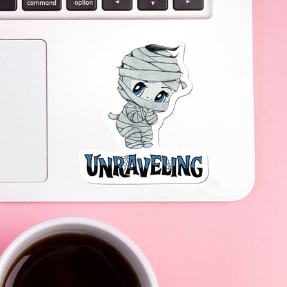 Creepy cute mummy sticker on a white laptop trackpad beside a cup of coffee