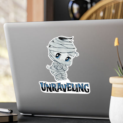 Large chibi mummy sticker with blue eyes and UNRAVELING lettering on the back of a silver laptop