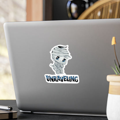 Medium chibi mummy sticker with blue eyes and UNRAVELING lettering on the back of a silver laptop