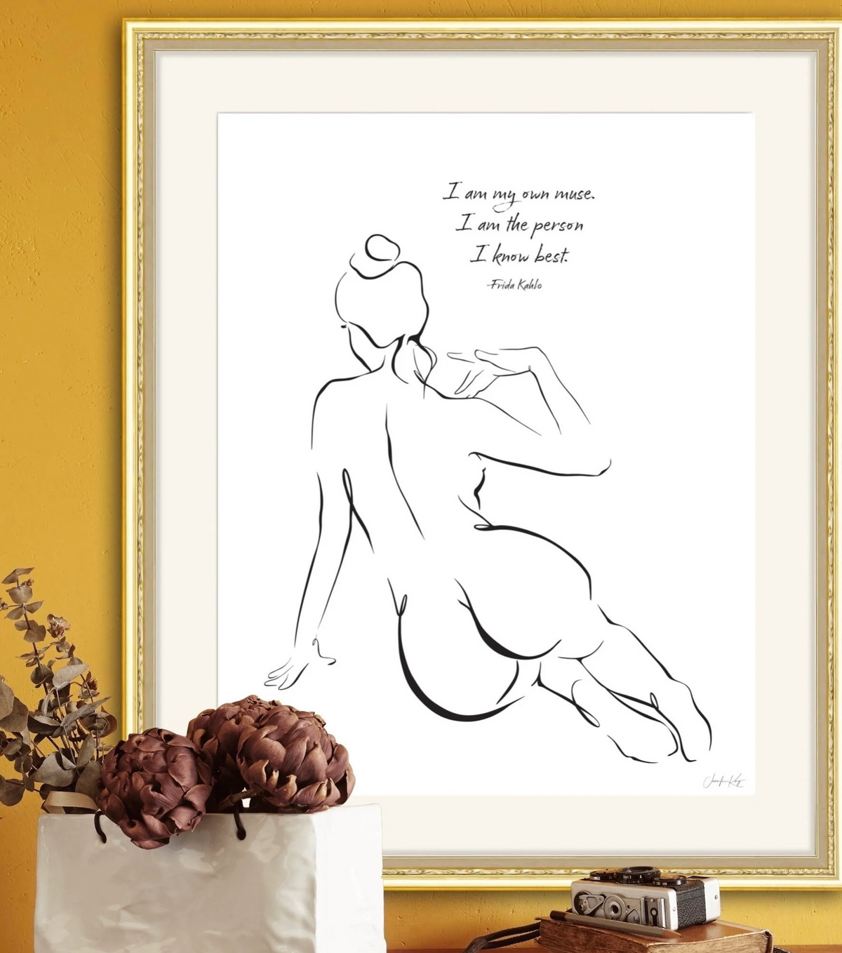 Black and white sensual line art print of a woman sitting with the quote "I am my own muse. I am the person I know best. - Frida Kahlo" in a cream mat and gold frame. 