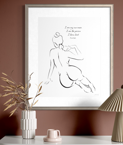 A framed wall art print featuring a sensual line drawing of a seated woman viewed from behind. The text reads: I am my own muse. I am the person I know best. Frida Kahlo. The artwork is presented in a thin metallic gold frame with a white mat.