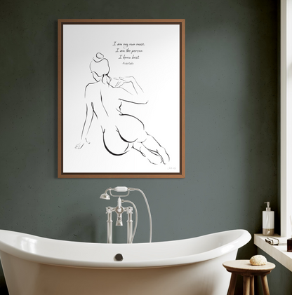 An oak framed wall art print featuring a sensual line drawing of a seated woman viewed from behind. The text reads: I am my own muse. I am the person I know best. Frida Kahlo. Elegant bathroom setting with artwork on a green wall over a traditional bath tub. 