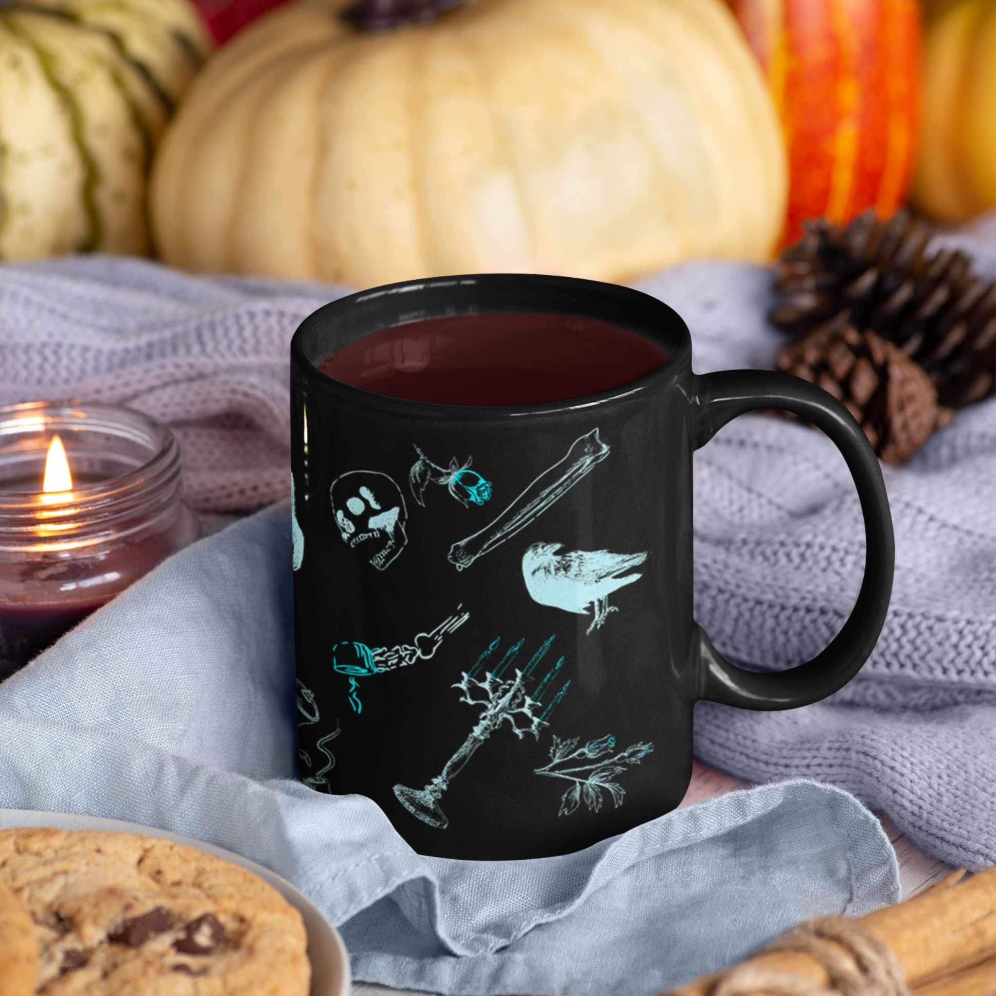 Black neon goth mug filled with dark coffee on a lavender knit throw beside pumpkins, a lit candle, and cookies