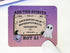 A rectangular desk mat with a purple and pink gradient background, featuring a gothic-style Ouija board design with the text &