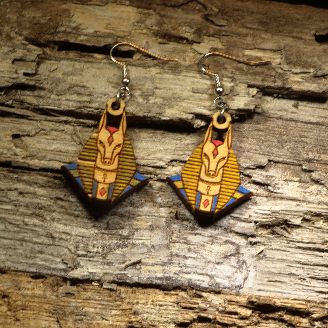 Hand-painted wooden Anubis dangle earrings featuring the jackal-headed Egyptian god with detailed ancient Egyptian artwork. Crafted from lightweight wood with hypoallergenic .925 sterling silver hooks, these mythological earrings are perfect for history lovers, Egyptology enthusiasts, mythology fans, museum gift shoppers, gothic fashion, and anyone who appreciates ancient civilization-inspired jewelry.