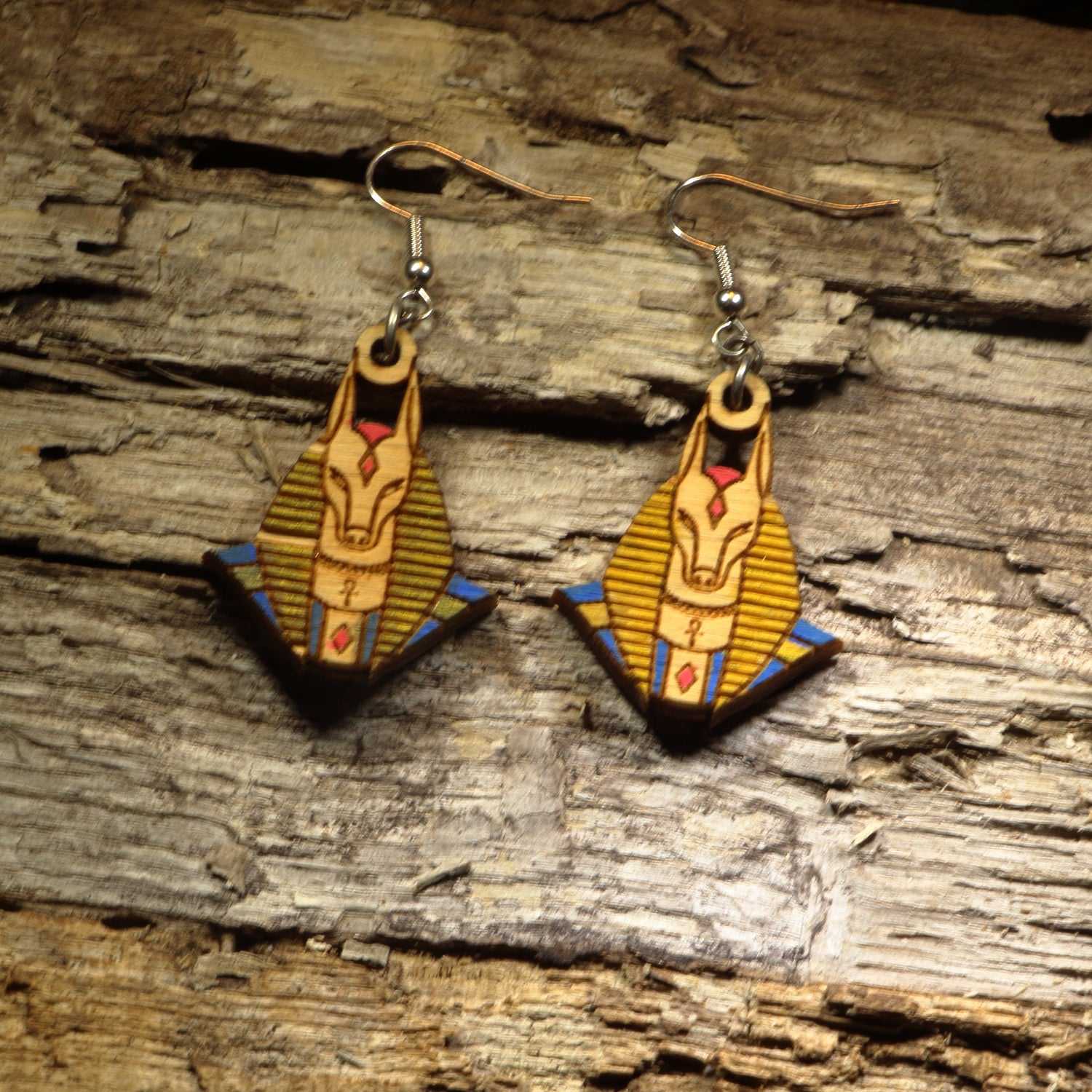 Hand-painted wooden Anubis dangle earrings featuring the jackal-headed Egyptian god with detailed ancient Egyptian artwork. Crafted from lightweight wood with hypoallergenic .925 sterling silver hooks, these mythological earrings are perfect for history lovers, Egyptology enthusiasts, mythology fans, museum gift shoppers, gothic fashion, and anyone who appreciates ancient civilization-inspired jewelry.