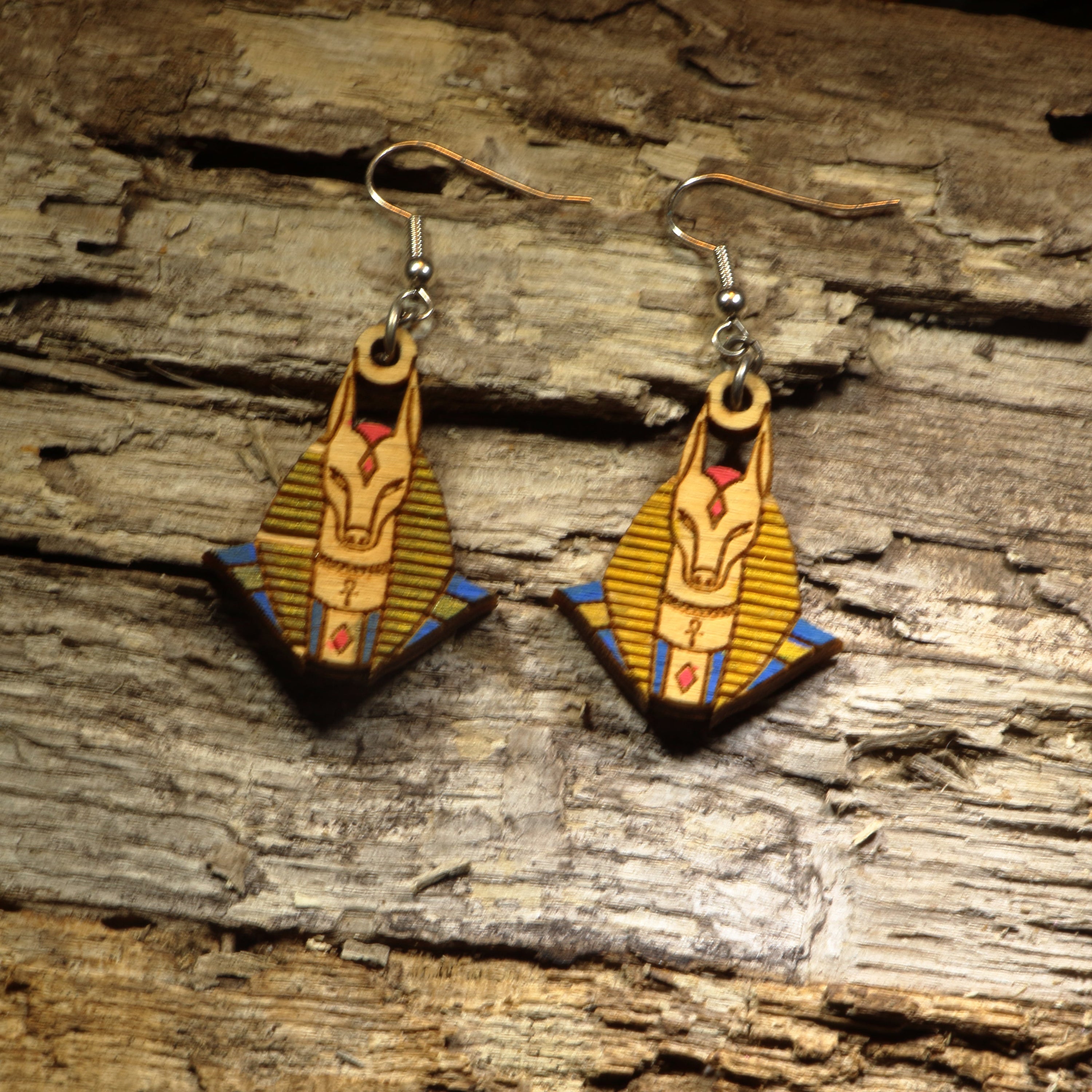 Hand-painted wooden Anubis dangle earrings featuring the jackal-headed Egyptian god with detailed ancient Egyptian artwork. Crafted from lightweight wood with hypoallergenic .925 sterling silver hooks, these mythological earrings are perfect for history lovers, Egyptology enthusiasts, mythology fans, museum gift shoppers, gothic fashion, and anyone who appreciates ancient civilization-inspired jewelry.