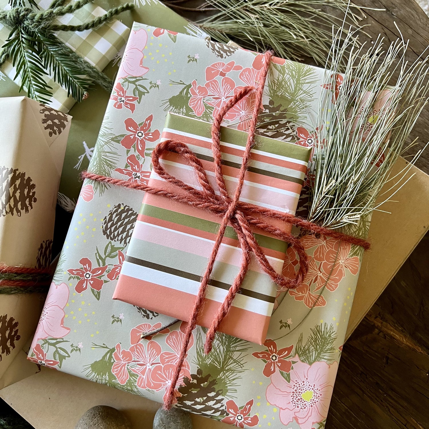 Giftwrapped package with two boxes, one in a pink &amp; olive floral pattern with pinecones, one in a pink &amp; olive stripe