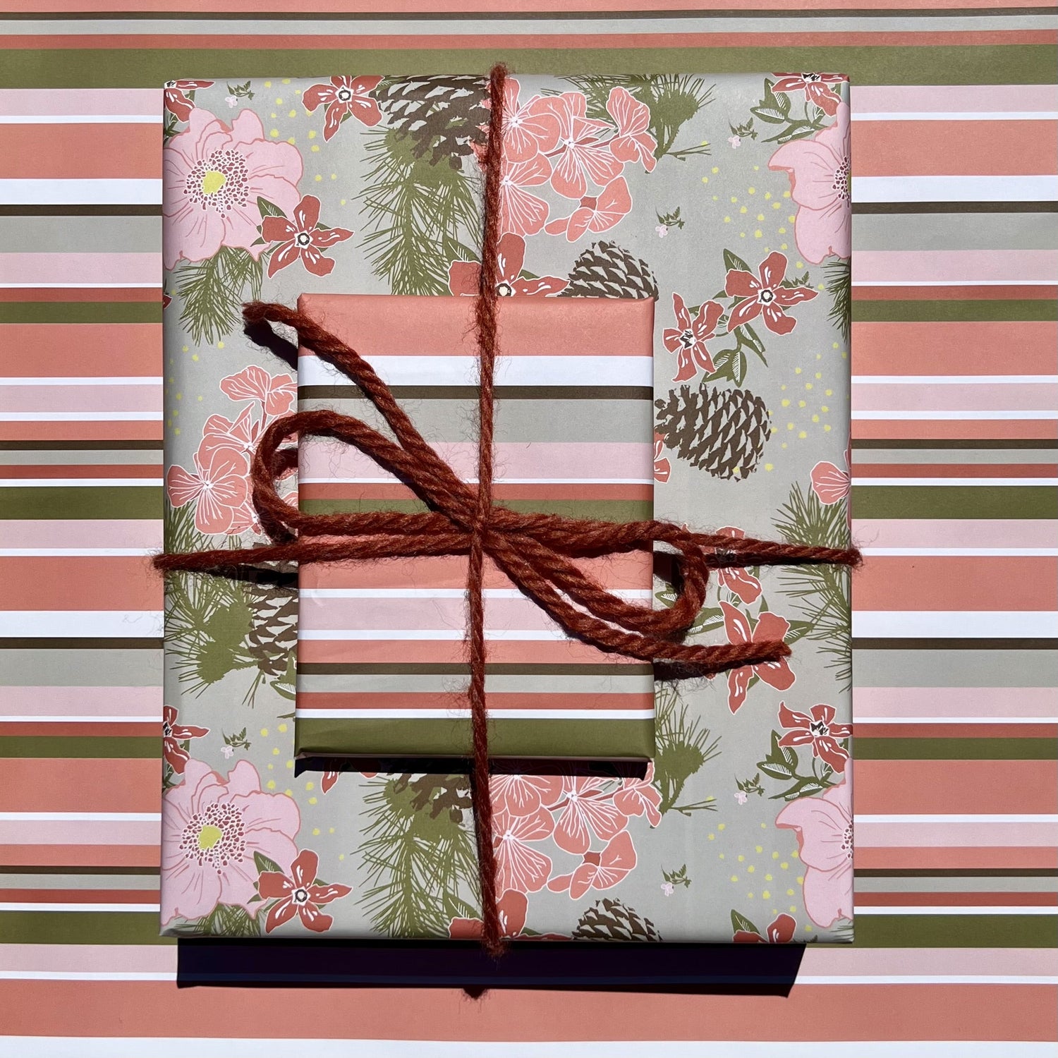 Giftwrapped package with two boxes, one in a pink &amp; olive floral pattern with pinecones, one in a pink &amp; olive stripe