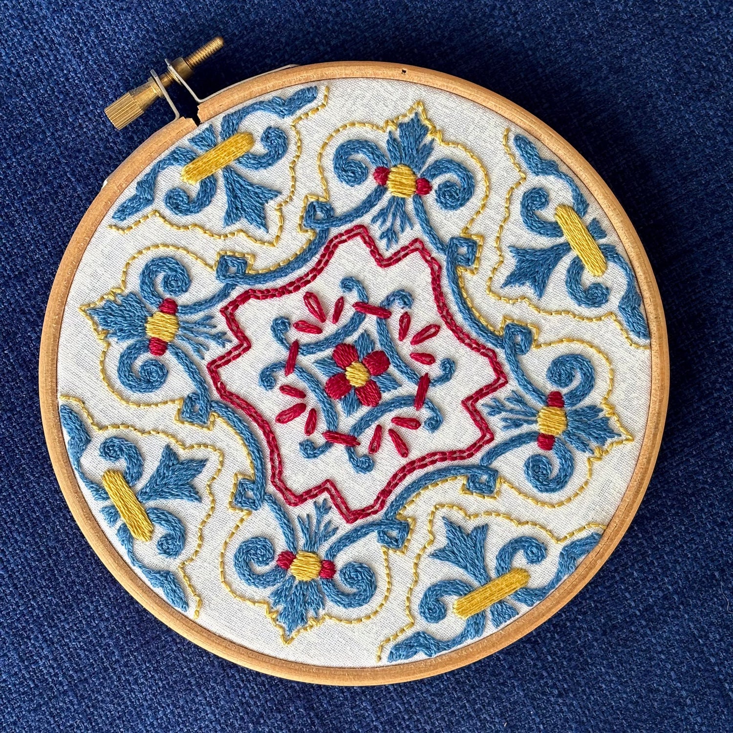 Blue, red, and yellow embroidery based on traditional Portuguese tile. Fabric is white on white cotton. Embroidery is displayed as wall art in light wood embroidery hoop.