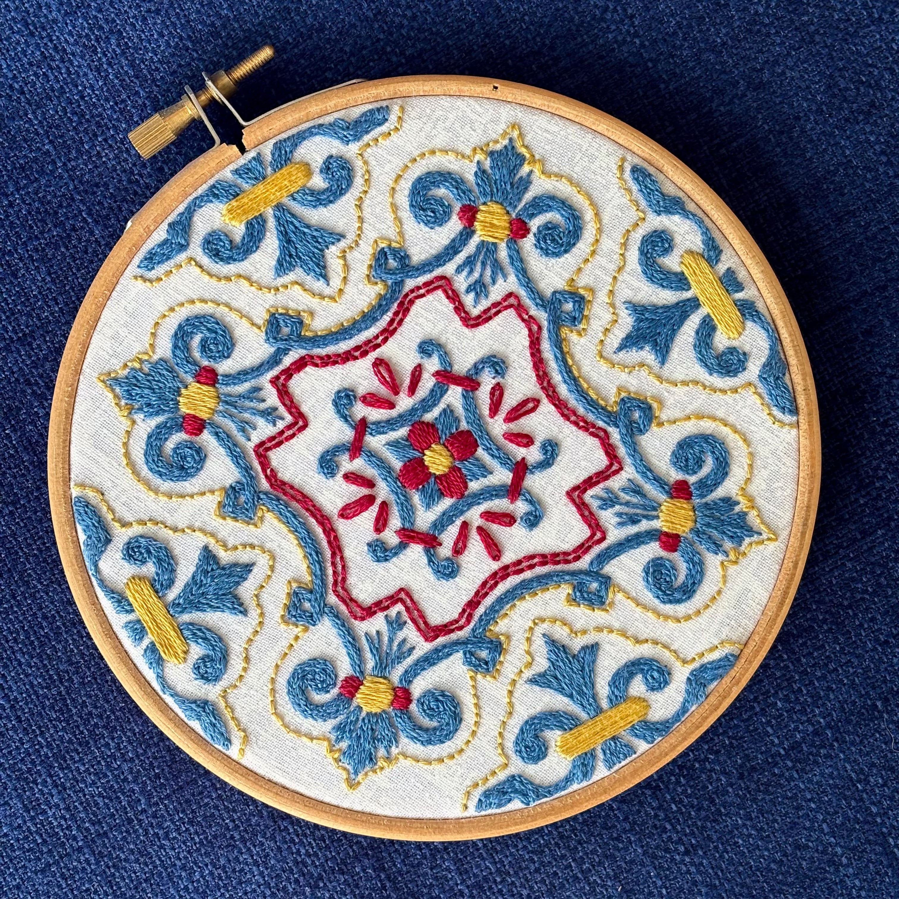 Blue, red, and yellow embroidery based on traditional Portuguese tile. Fabric is white on white cotton. Embroidery is displayed as wall art in light wood embroidery hoop.